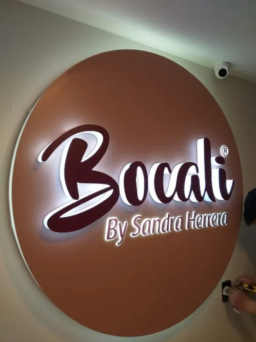 Aviso circular retroiluminado instalado en pared interior, con el logotipo en letra manuscrita recortada que deja pasar la luz led.