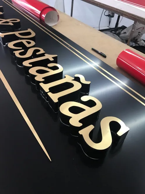 Letras corpóreas con cuerpo negro y frente dorado, alineadas sobre la mesa del taller antes de montarlas.