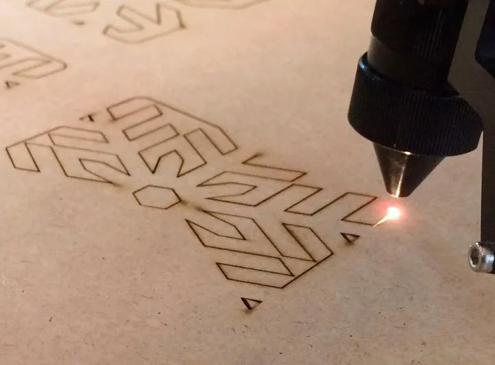 Láser grabando un patrón geométrico sobre una lámina de MDF, con el trazo quemado ya visible.
