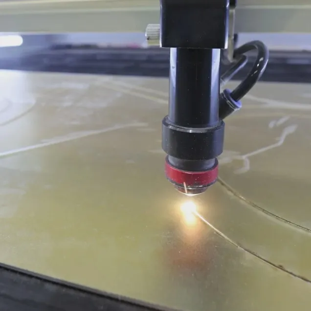 Cabezal de corte láser trabajando sobre una lámina de acrílico dorado, con el punto de corte encendido.