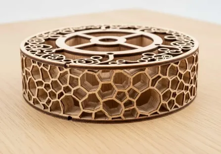 Caja circular de madera cortada a láser con un patrón de celdas hexagonales calado en toda la pared exterior.