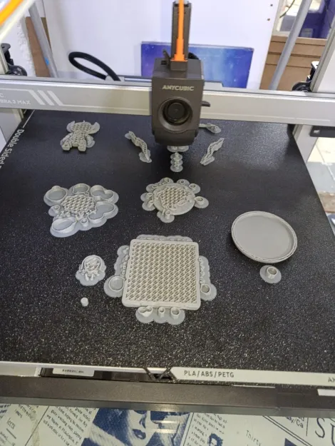 Cama de la impresora de filamento con varias piezas grises recién terminadas, incluida una placa con relleno en panal a la vista.